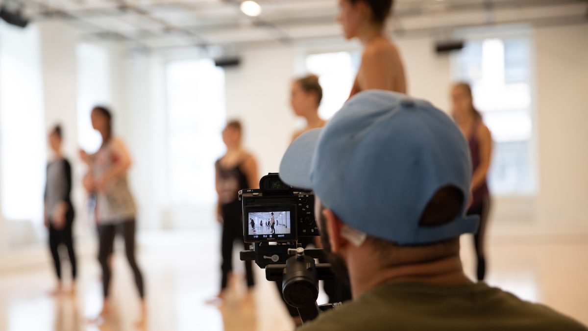 Person filming a group of dancers. The dancers are blurry and the camera is in focus.