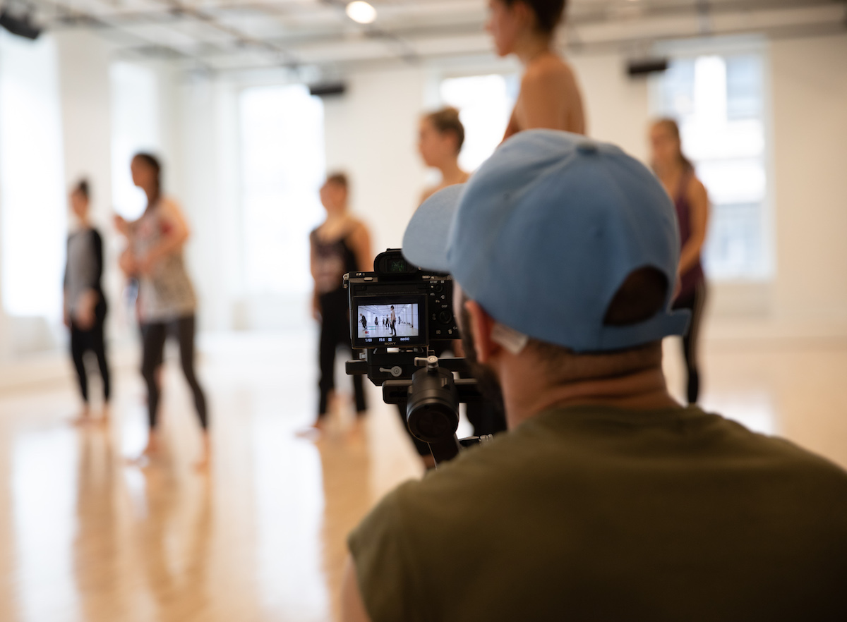 Person filming a group of dancers. The dancers are blurry and the camera is in focus.