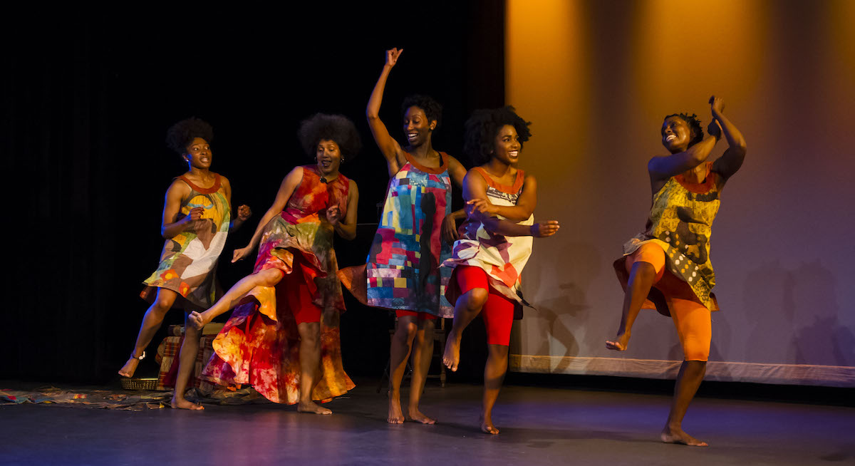 Group of black women smiling and dancing together on stage.
