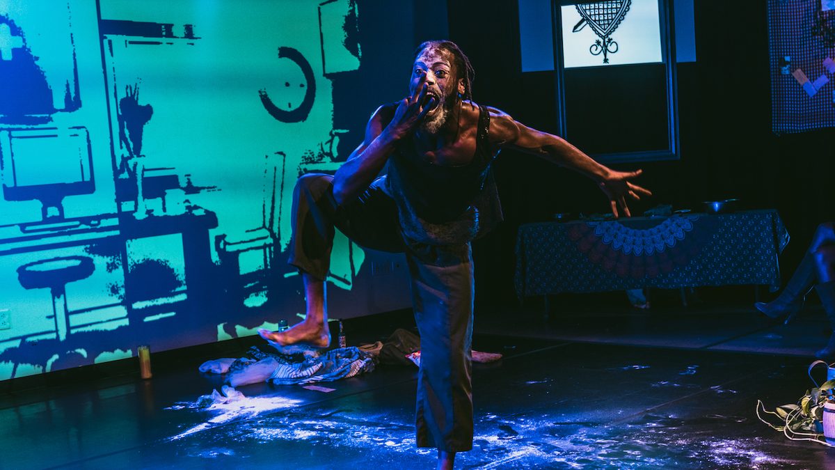 Black man mid-motion on stage yelling with his hand close to his mouth.