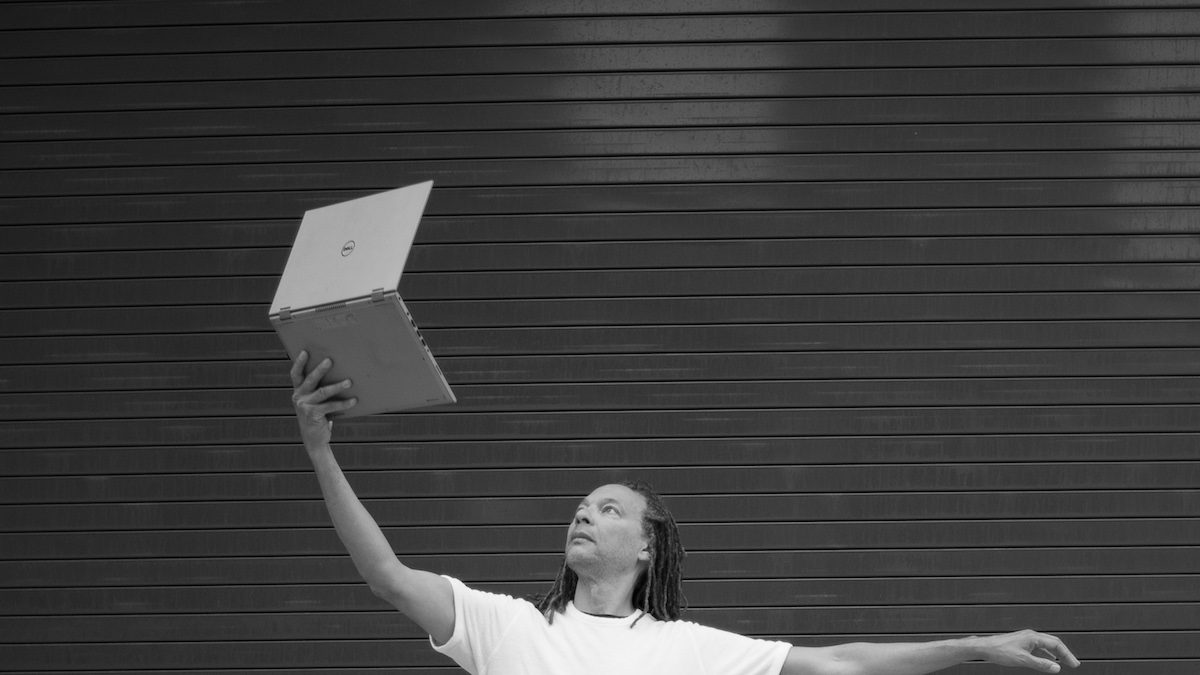 Man in a dance position holding a laptop in the air.