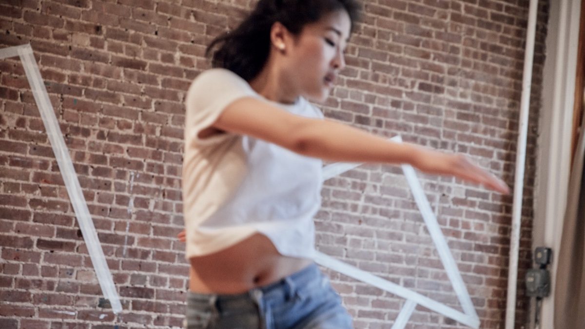 Blurred asian woman in motion in front of a brick wall.