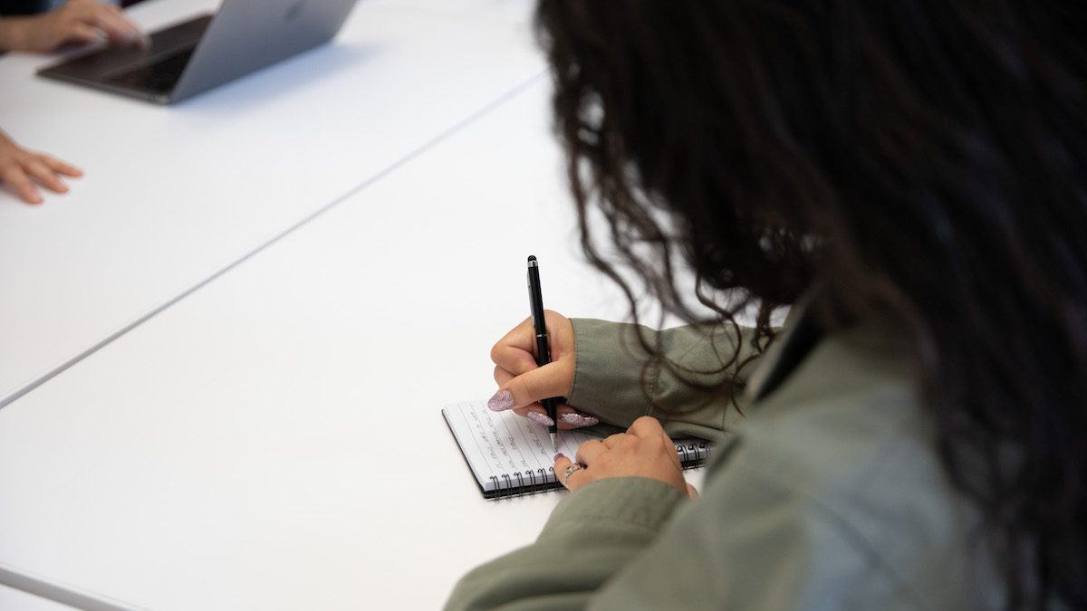 Woman writing in a notebook on a desk.