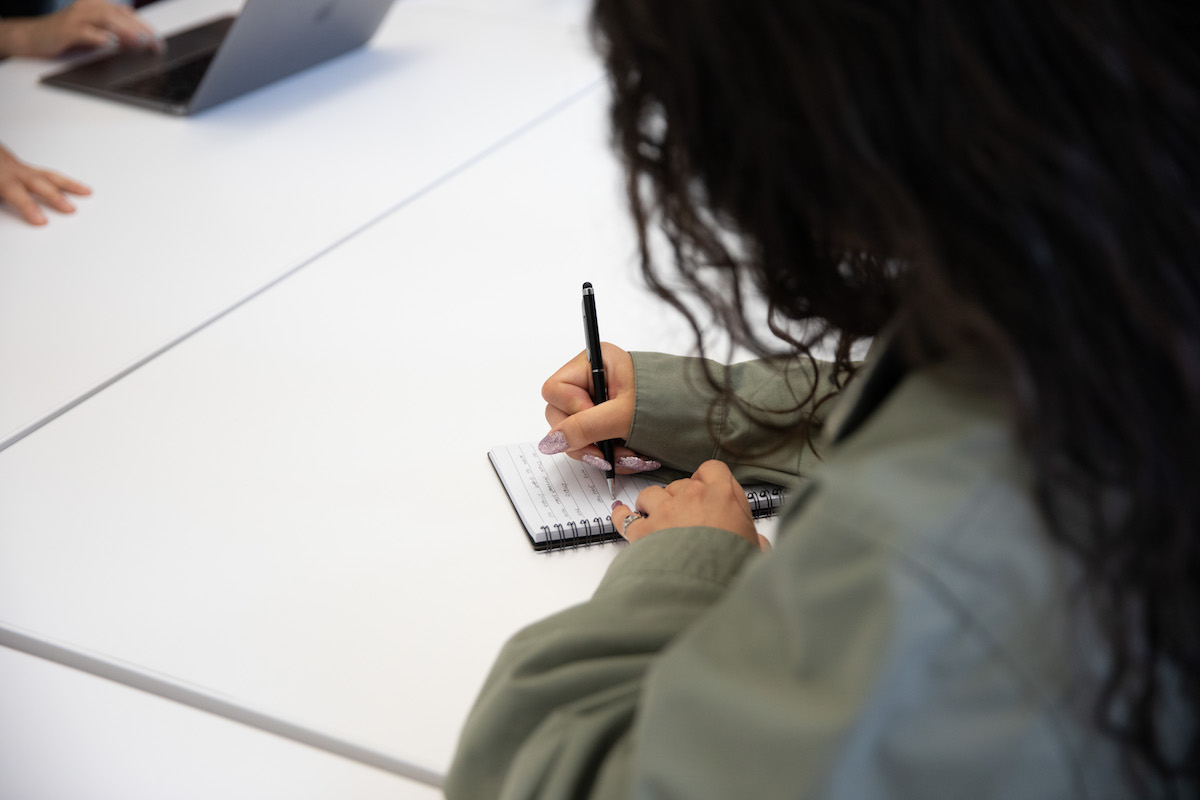 Woman writing in a notebook on a desk.