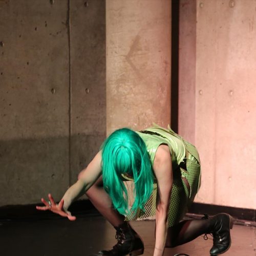 Leyya Mona Tawil as Lime Rickey International, crouching onstage with the right hand outstretched.