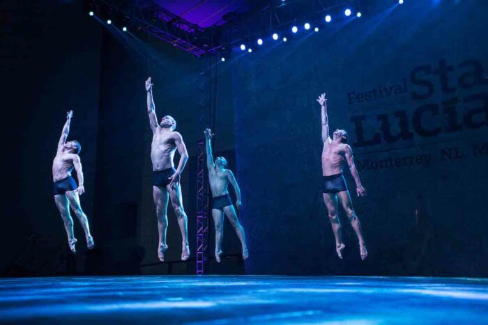 Group of men jumping in the air on stage with their right arms lifted high.