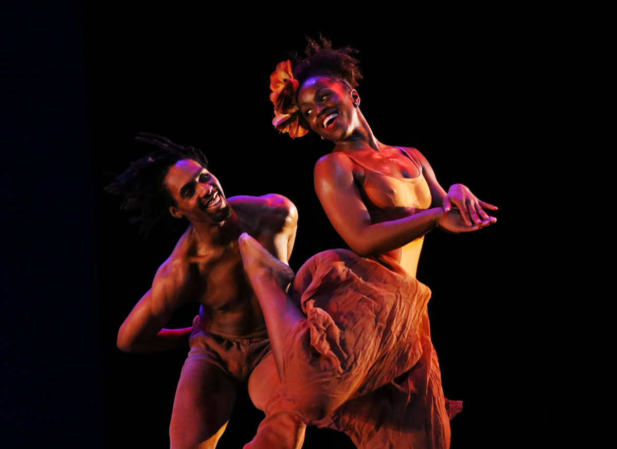 Two black dancers smiling and looking at each other on stage.