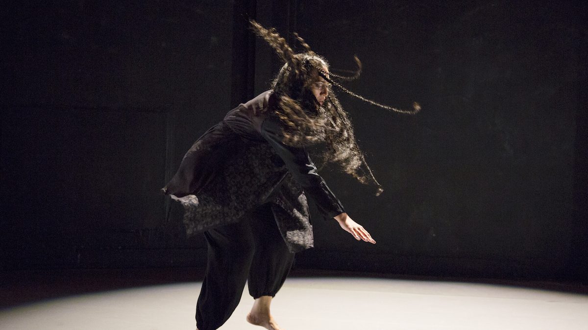 Woman dancing underneath a spotlight. Her hair flies in the air.