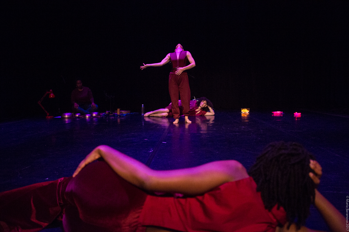 Group of people on stage. Some are laying down watching, and one is standing and performing.