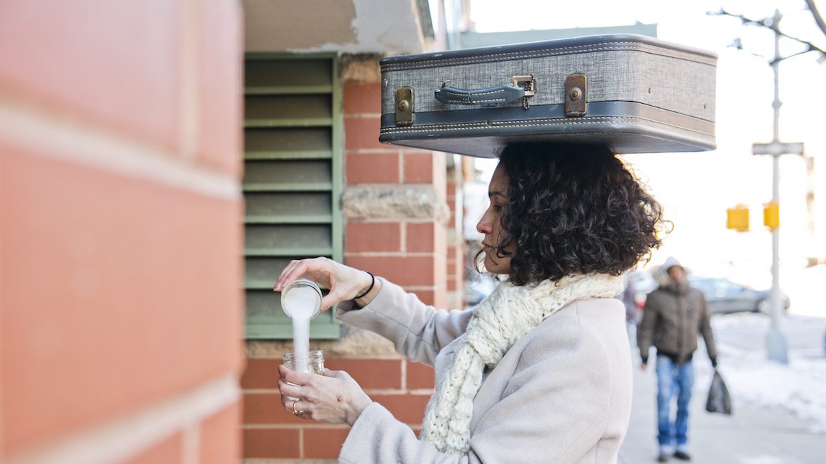 Woman balancing a suitcase on her head while she pours salt into a glass.