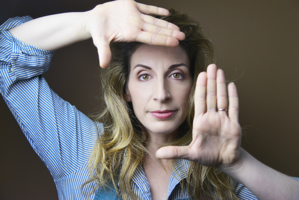 White woman with her hands framing her face as she looks into the camera.