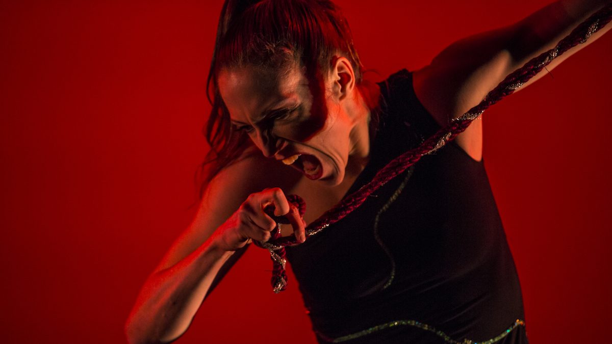 Woman saturated in red, with her mouth wide open, about to bite her hand.