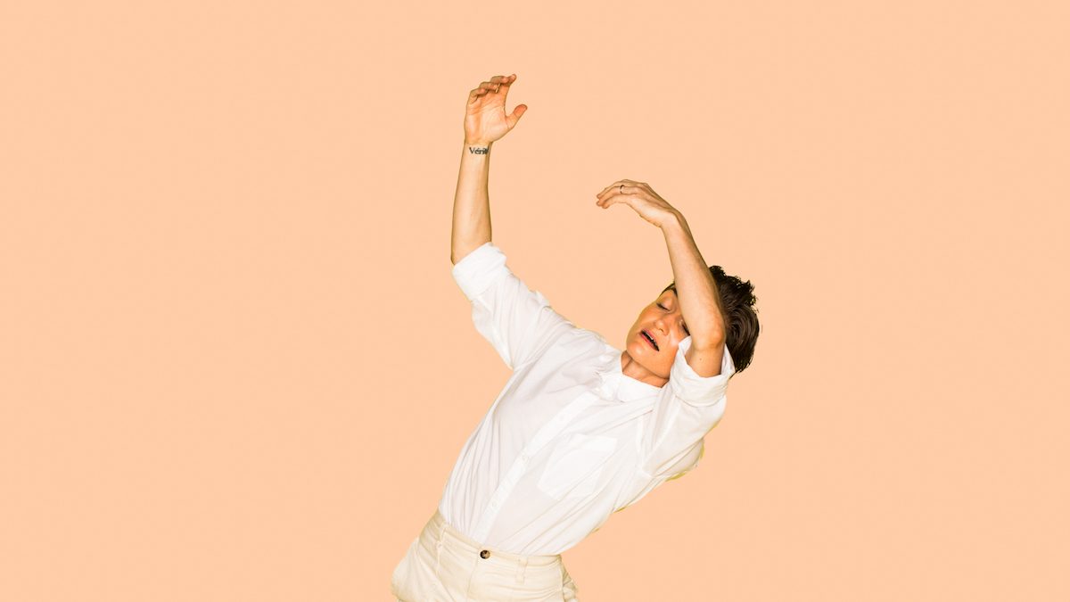 Woman in front of a peach background dancing.