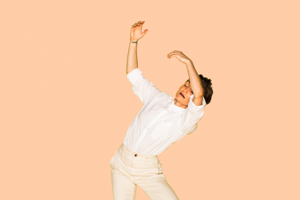 Woman in front of a peach background dancing.
