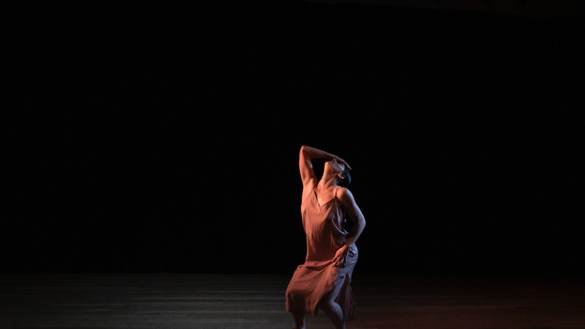 White woman with an arched back, looking up towards the ceiling while her arm covers her face.