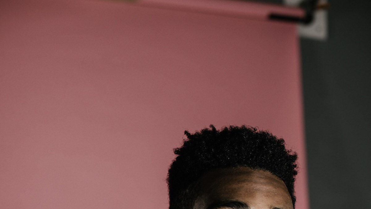 A Black man looking away from the camera in front of a pink backdrop.