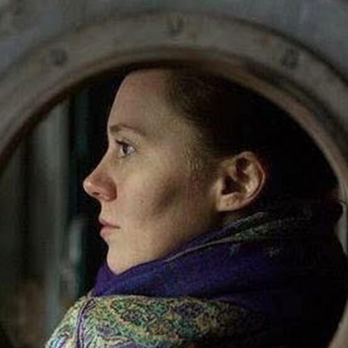 A photo of a woman through a circular window as she looks sideways.