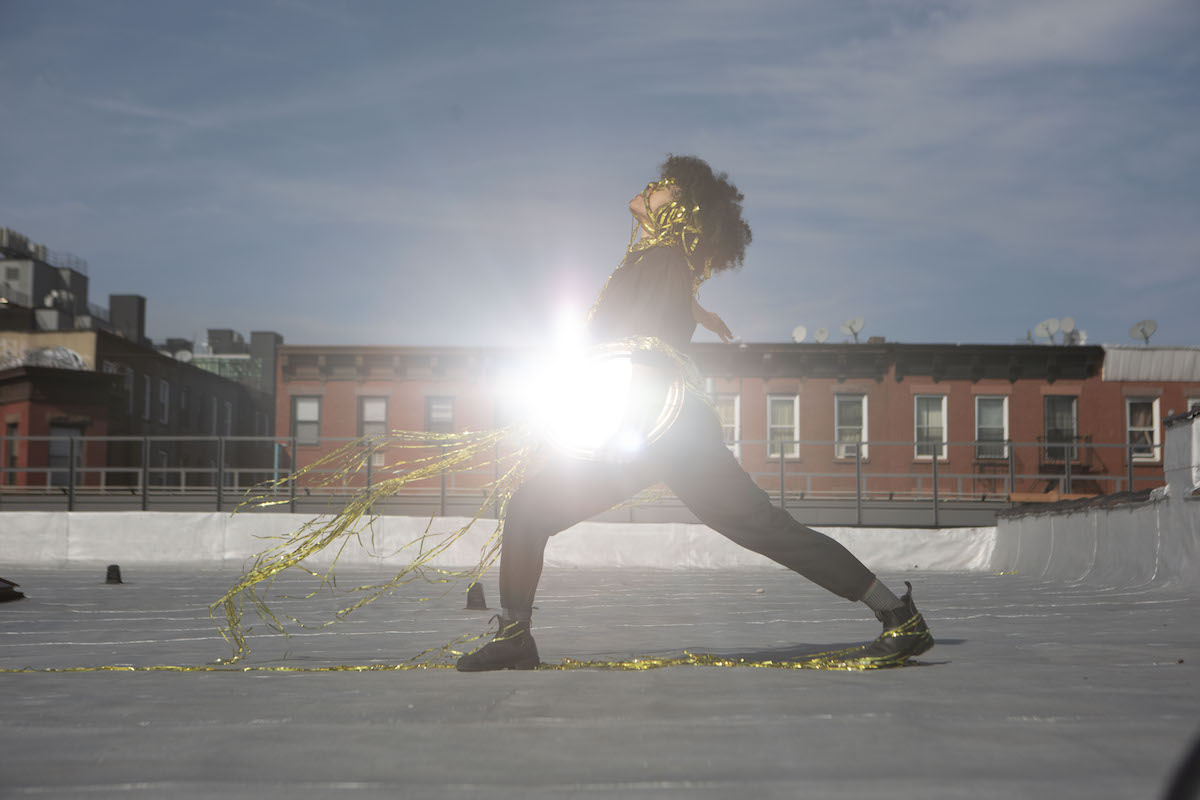 Woman on a roof holding a mirror as it shines light into the camera.