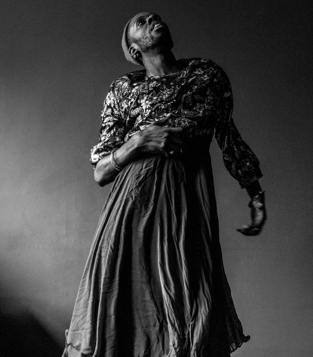 Black and white photo of a Black man elegantly posed in a dress.