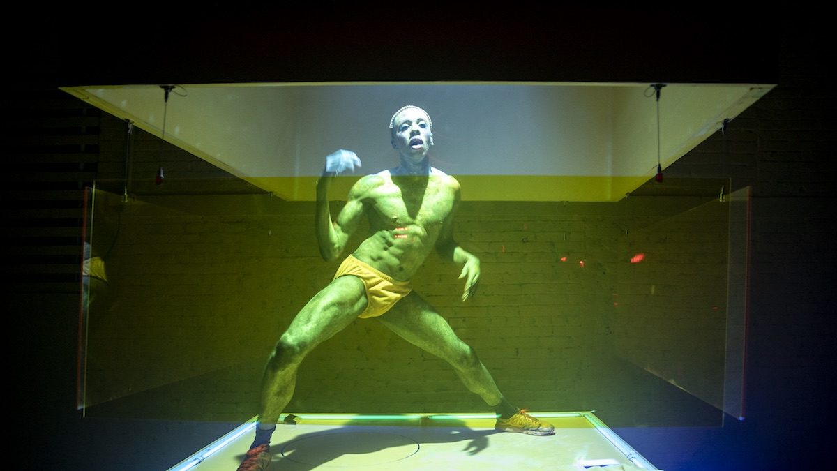 A black man in a neon green light dancing in a box.