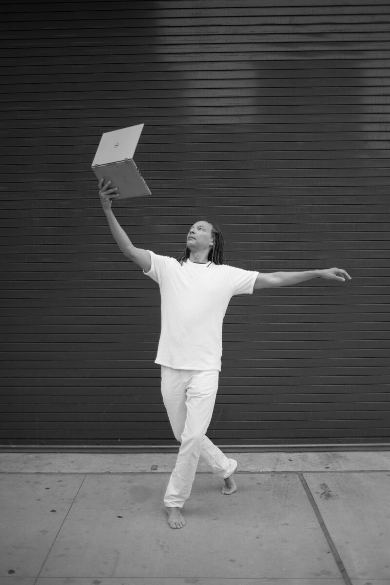 Man holding a laptop computer to the sky in a quaint pose.