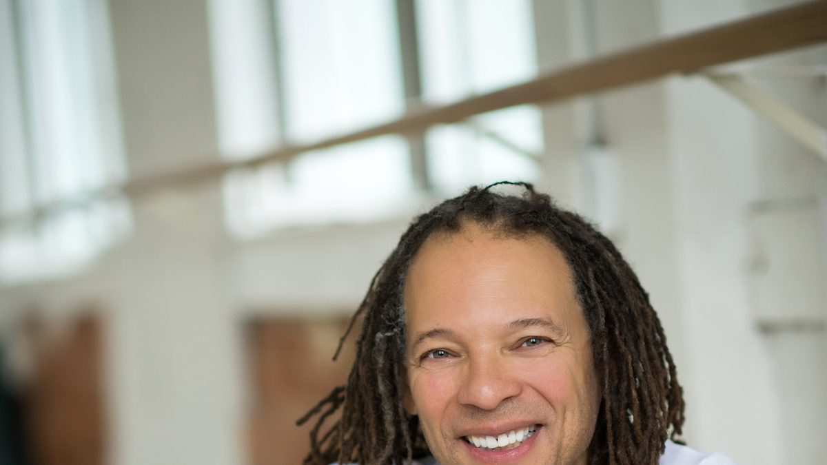 Black man smiling at the camera as he sits on a dance floor.