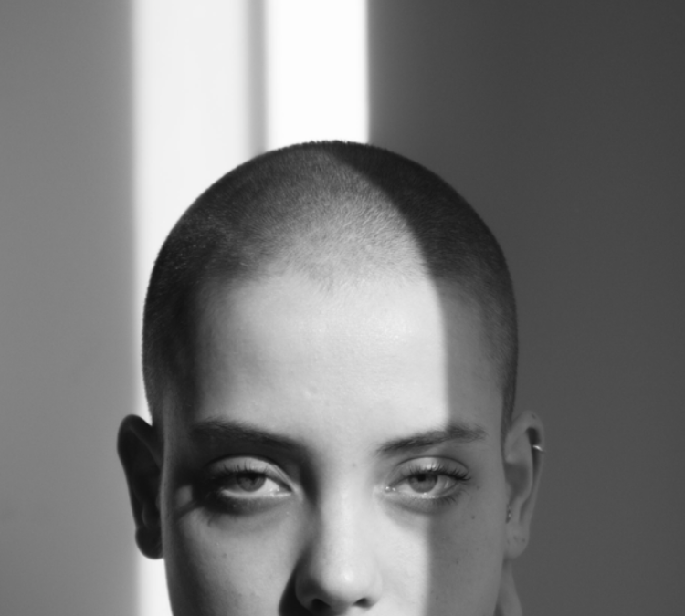 Black and white photo of a white woman with a shaved head looking at the camera.