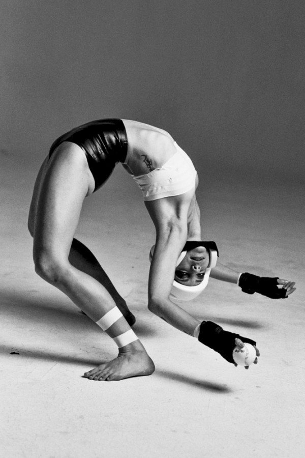 White woman holding a baseball in a deep backbend.