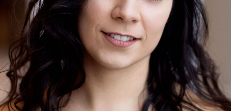 Bianca smiling towards the camera, with long dark brown curly hair, wearing a green tank top.