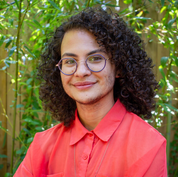 A person of color with curly brown hair and glasses smiling at the camera.