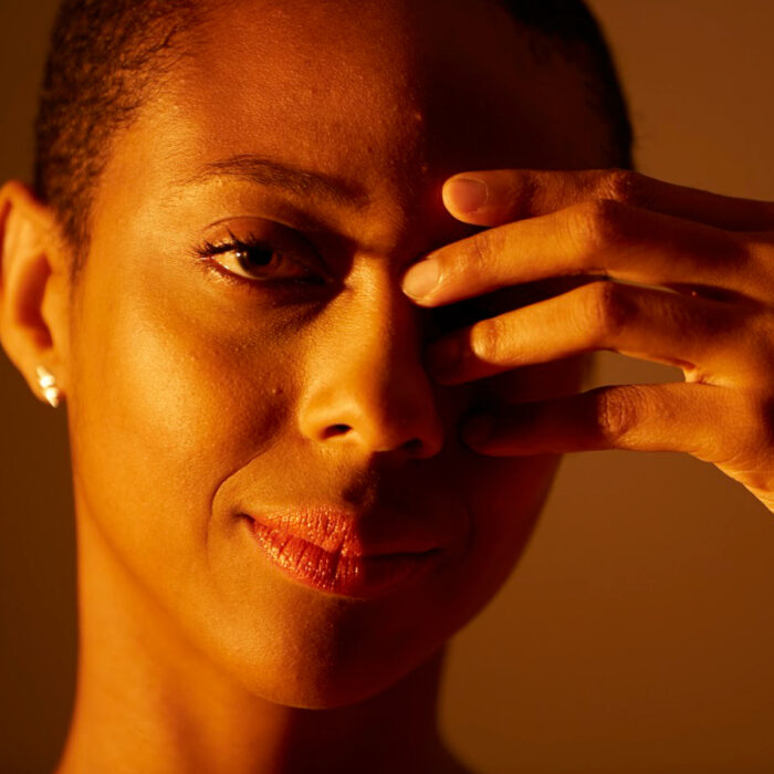 Black woman smiling at the camera with her hand covering one eye.