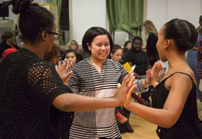 Two SLMDances artists (Kayla Hamilton and Kimberly Mhoon) and an audience member connect in a circle by pressing their palms together. They are smiling and sharing their weight.