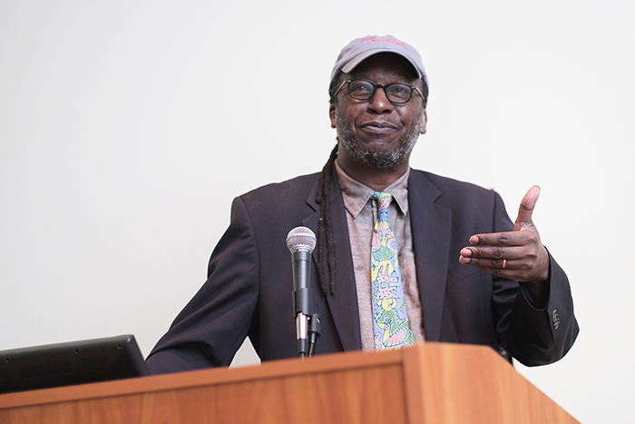 Cornelius Eady gestures from behind a podium as he speaks publicly.