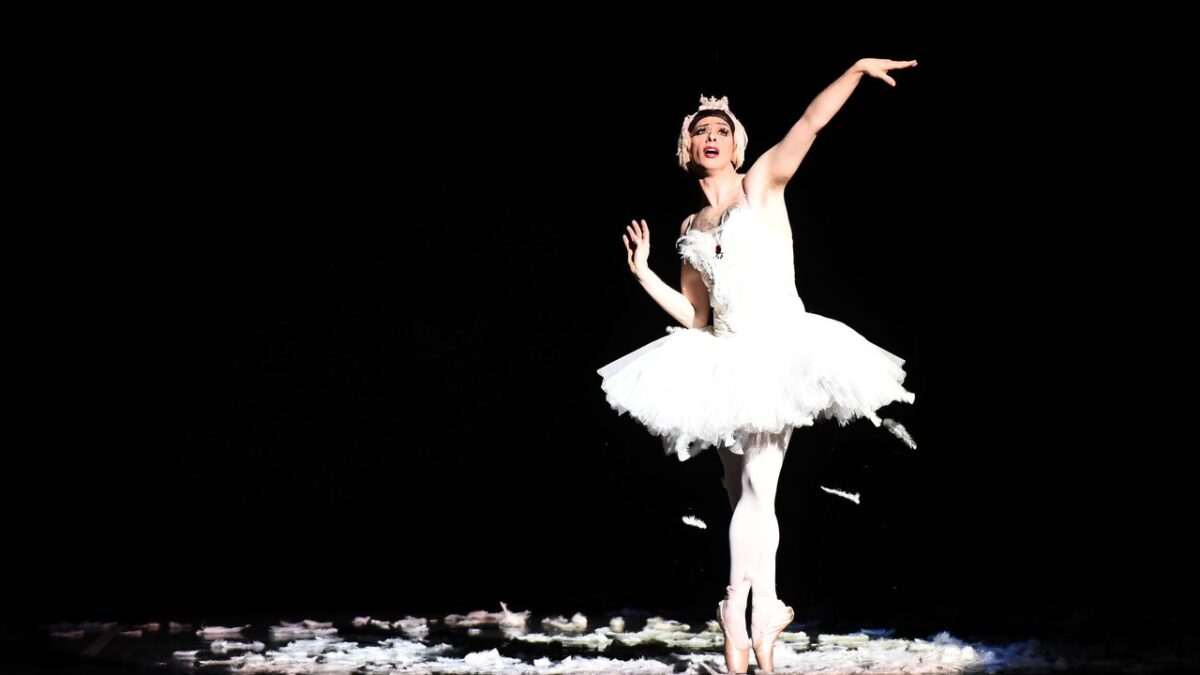 Full body picture of a ballerina in white in front of a black background