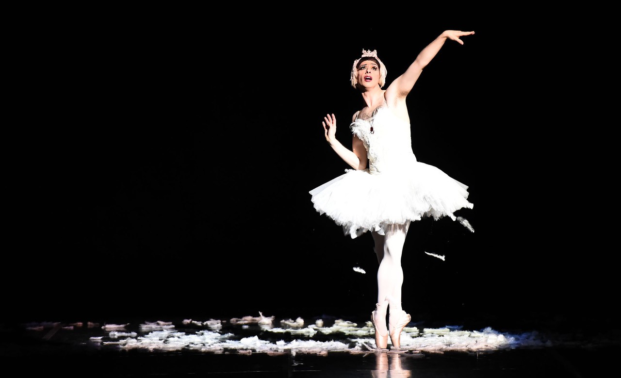 Full body picture of a ballerina in white in front of a black background