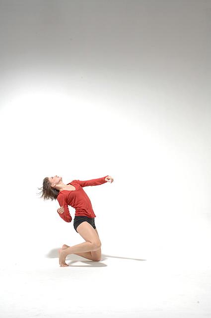 Wide shot of Giulia Carotenuto on the floor dancing in a red shirt in front of a white background