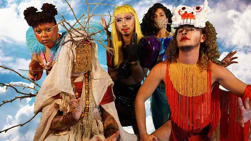 Five deities in colorful costume, masks, and drag look into the camera lens and pose boldly. Behind them is a digital backdrop of a blue sky.