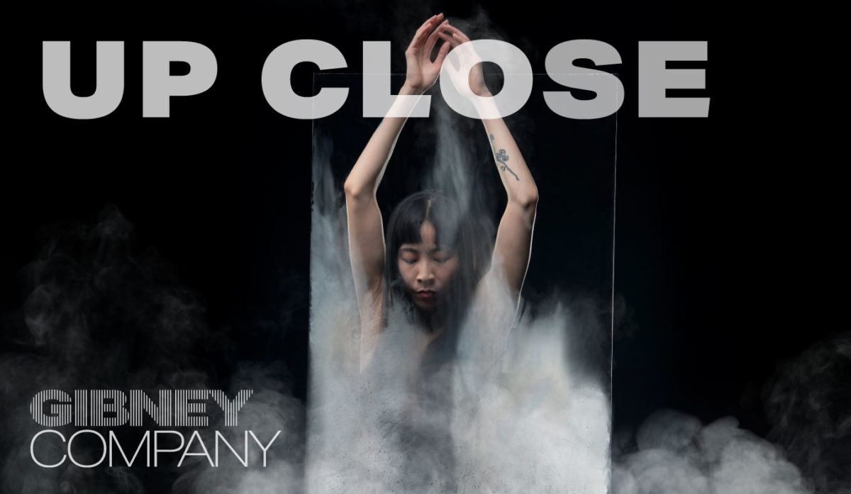 Photo of dancer Jie-Hung Connie Shiau against a black background, partially obscured by a piece of clear plexiglass and white smoke. She reaches upward with both arms while gazing down. Text reads UP CLOSE and the Gibney Company logo is in the bottom left corner.