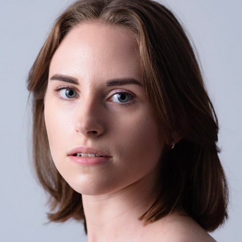 Headshot of Madeline Honegger, a white woman with shoulder length brown hair against a light grey background