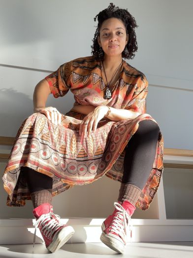 Light-skinned Black woman sits wearing a flowy earth-toned skirt and shirt set and red Converse sneakers. Photo by Imagine Photography - Kea Taylor.