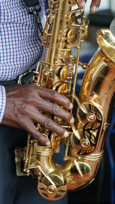 Image Description: Closeup of a jazz musician in a plaid dress shirt playing the Saxophone.